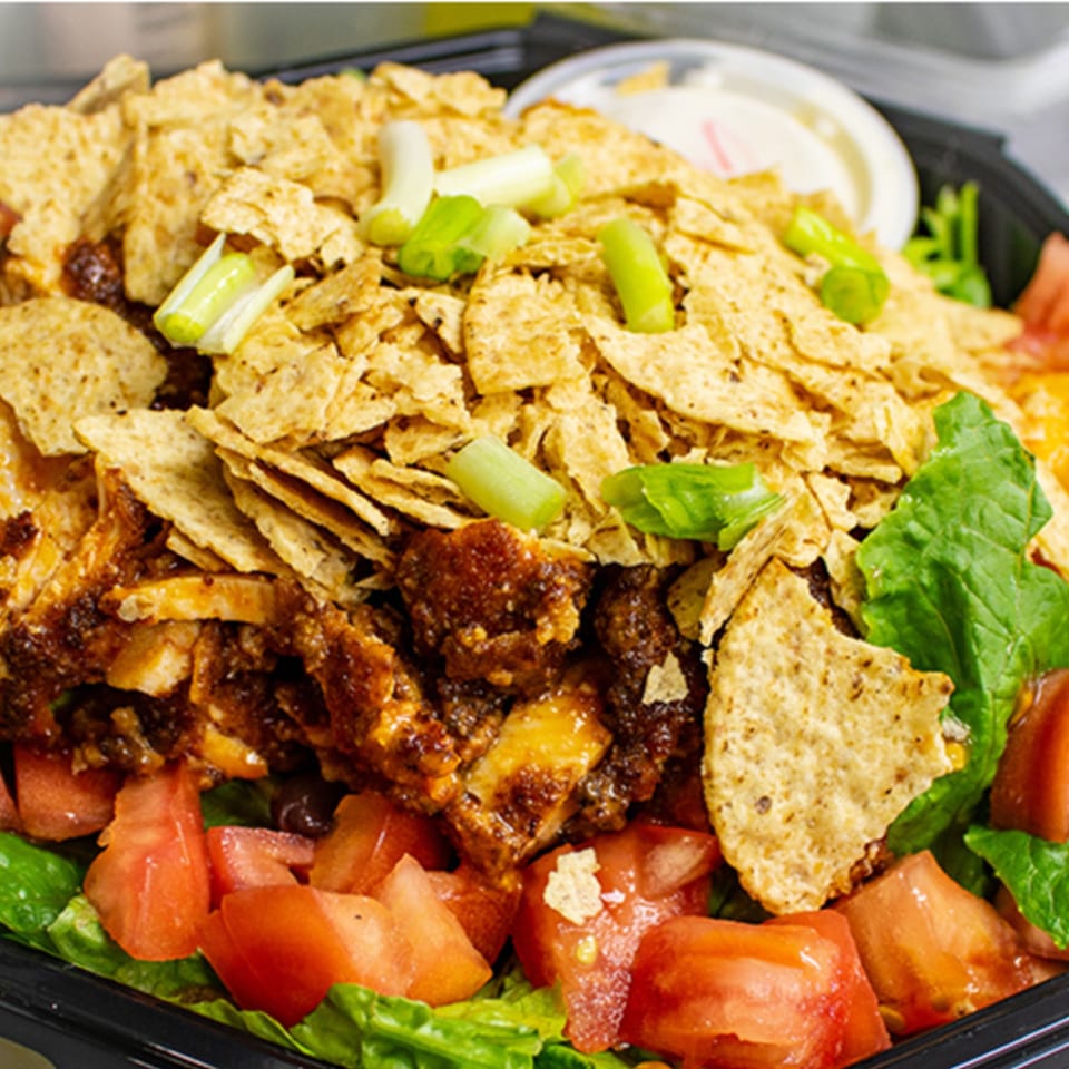 A Capitini's Italian Deli taco salad with seasoned meat, lettuce, tomatoes, chips, and green onions.