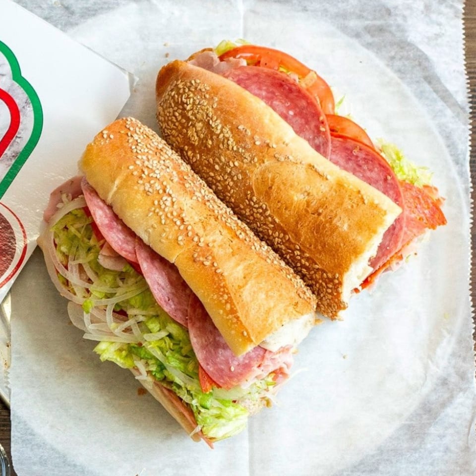 Two halves of a Capitini's Italian Deli sandwich with meats, lettuce, onions, and tomatoes.