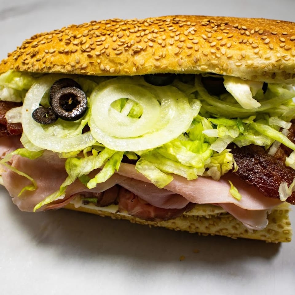 Close-up of a Capitini's Italian Deli sub sandwich with ham, lettuce, onions, and olives.
