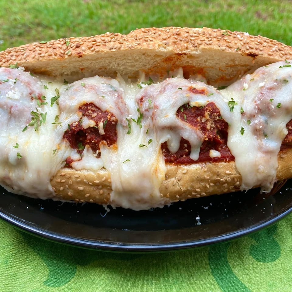 A Capitini's Italian Deli meatball sub with melted mozzarella cheese and parsley on a black plate.