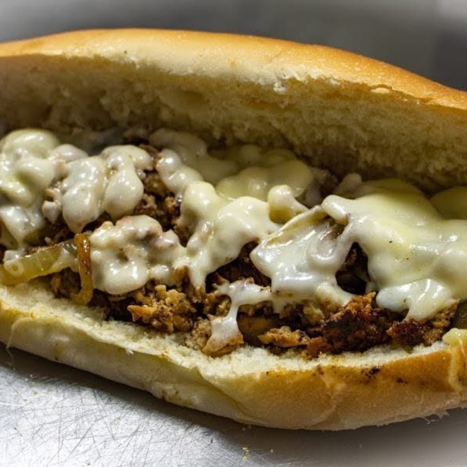 Close-up of a Capitini's Italian Deli cheesesteak sandwich with melted cheese and onions.